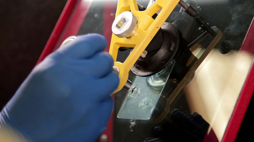 A gloved hand uses a specialized tool to repair a crack in a windshield, showcasing the precision skills gained from PDR training in California.