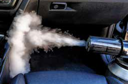 A device emits a dense spray into the interior of a car, appearing to release smoke or steam near the passenger seat dashboard—a common sight during PDR Training in California.