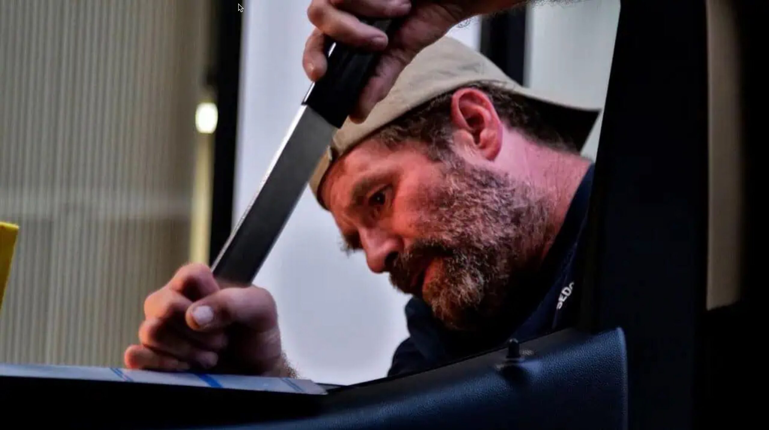 A bearded man wearing a cap, likely involved in PDR Training in California, uses a tool to pry open an object, focusing intently on the task.