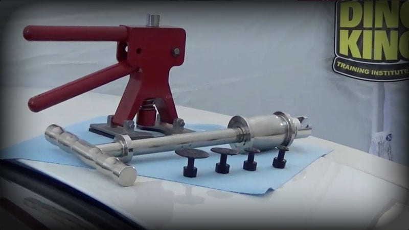 A red metal lever device and several cylindrical metal tools are arranged on a blue cloth placed on a white surface, with a sign partially visible in the background, showcasing equipment used in PDR Training in California.