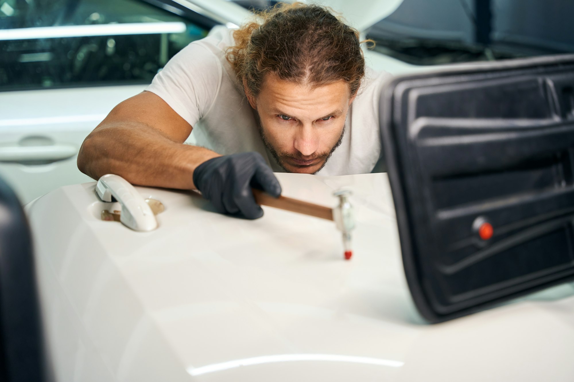 Guy smoothes out dents on door of a white car