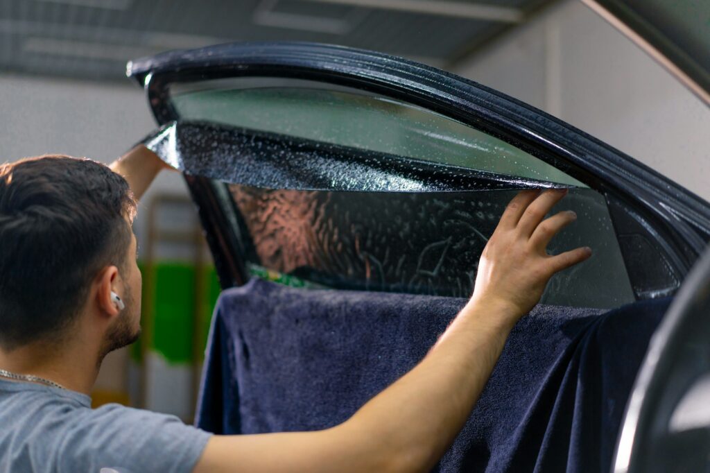 Male car service worker glue window tinting in luxury car detailing car repair