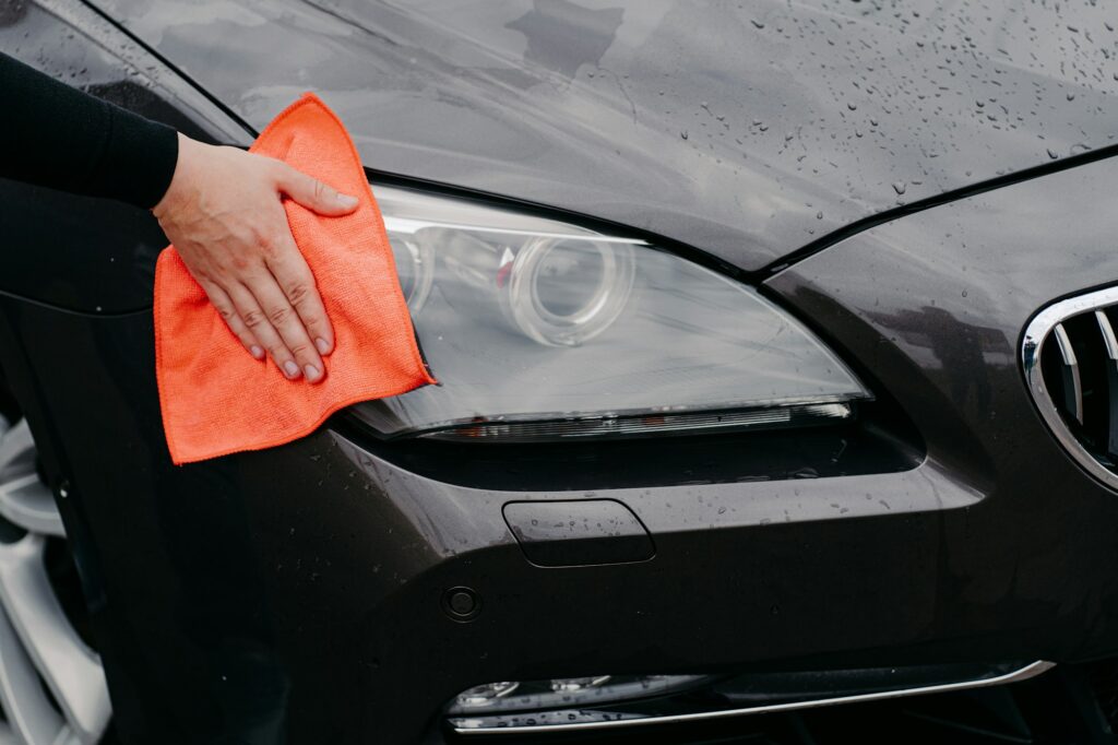 Mans hand wiping car headlight with microfiber cloth. Automobile detailing