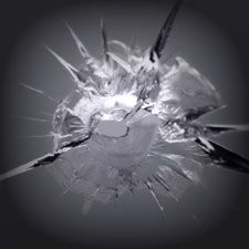 A close-up image of a cracked and shattered glass surface in grayscale. The glass is broken into sharp, jagged fragments radiating from a central point, resembling the precision often mastered in PDR Training in California.