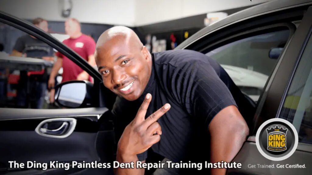 A man smiles and flashes a peace sign while leaning out of a car door. The text reads "The Ding King Paintless Dent Repair Training Institute" and "Get Trained. Get Certified with PDR Training Courses.