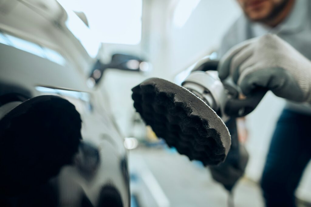 Close-up worker polishing car at auto service workshop.